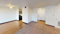 Located at 34 S Main Street in Wilkes-Barre, Pennsylvania, this single-floor unit offers a practical and straightforward layout designed for comfortable everyday living. The floor plan, visible in the 3D overview, reveals a well-organized arrangement of living, kitchen, and private spaces connected by clear, accessible pathways.

The living area is generously sized, featuring neutral-toned carpet and cream-colored walls that create a clean, understated atmosphere. Multiple windows allow natural light to filter in, offering views of the surrounding urban environment. Vertical blinds on a sliding door provide additional light control and access to an exterior area.

The kitchen is equipped with dark wood cabinetry offering ample storage, light-toned countertops, a stainless sink, and black appliances including an electric range, dishwasher, and refrigerator. The kitchen flows openly toward the living space, enhancing the overall sense of connectivity. Warm hardwood-style flooring runs throughout the kitchen and entry areas.

The bathroom features a full tub-shower combination with white tile surround, chrome fixtures, and a grab bar for added safety. The space maintains a clean, functional aesthetic with tile flooring. Overall, the unit presents a practical, move-in ready environment in a central Wilkes-Barre location.