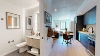 Located in the heart of downtown Phoenix, this contemporary studio offers an efficient, thoughtfully designed layout that maximizes every square foot. The open-plan living, dining, and kitchen area forms the core of the space, bathed in natural light through expansive floor-to-ceiling windows that frame striking views of the Phoenix skyline. Exposed concrete ceilings lend an industrial edge, complemented by light hardwood flooring that runs throughout the main living area.

The kitchen is outfitted with sleek, dark flat-front cabinetry, a white tile backsplash, stainless steel appliances including a gas range, microwave, dishwasher, and refrigerator, as well as a matte black faucet over a deep sink. A compact dining area with a round table sits adjacent to the kitchen, creating a natural flow into the living space.

The sleeping area benefits directly from the large windows, filling the space with abundant natural light and commanding downtown views. The bathroom features large-format tile flooring, a frameless glass walk-in shower with white tile surround, and a floating vanity with a light wood finish. Additional conveniences include an in-unit laundry area and a dedicated closet, ensuring practical storage within this well-appointed urban residence.