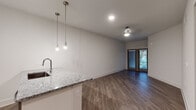 This single-floor residence is designed with a clean, modern aesthetic that emphasizes an open and cohesive layout. The combined kitchen and living area forms the heart of the unit, where dark hardwood-style flooring runs continuously throughout, grounding the bright, neutral-toned walls. The kitchen is outfitted with white shaker cabinetry, granite countertops, a subtle tile backsplash, and a full suite of stainless steel appliances, including an electric range, over-the-range microwave, and refrigerator. A peninsula with an undermount sink and pendant lighting overhead defines the boundary between the kitchen and the open living space. The living area is finished with a ceiling fan and recessed lighting, and is anchored by a set of French doors that allow natural light to filter in while providing outdoor access. The bedroom is a well-proportioned, quiet retreat with a window offering natural light and direct access to a closet. The bathroom features a tub-shower combination with large-format marble-style tile surround, granite vanity top, and wood-tone flooring, maintaining the consistent design language found throughout the unit.