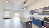 This thoughtfully designed two-story residence offers 1 bedroom and 2 bathrooms across two well-proportioned floors. The main level is anchored by an open-concept kitchen and living area, where light hardwood flooring and crisp white walls create a bright, contemporary atmosphere. The kitchen is a standout, featuring bold navy blue cabinetry, white subway tile backsplash, granite countertops, a large center island with pendant lighting, and a full suite of stainless steel appliances including a French door refrigerator. A sliding glass door in the living area provides direct access to a balcony with views of the surrounding neighborhood, filling the space with natural light. Bold navy baseboards and door trim add a distinctive design accent throughout. The upper level houses the spacious primary bedroom, which benefits from its own sliding glass door to an outdoor balcony, a ceiling fan, and generous proportions. A closet provides dedicated storage. Both bathrooms echo the home's design language with navy vanities, granite countertops, and modern fixtures. One bathroom features an angled ceiling, adding architectural character. The layout also includes a dedicated staircase connecting both levels, rounding out a well-appointed and cohesive living space.