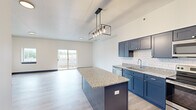 This thoughtfully designed two-story residence offers 1 bedroom and 2 bathrooms across two well-proportioned floors. The main level is anchored by an open-concept kitchen and living area, where light hardwood flooring and crisp white walls create a bright, contemporary atmosphere. The kitchen is a standout, featuring bold navy blue cabinetry, white subway tile backsplash, granite countertops, a large center island with pendant lighting, and a full suite of stainless steel appliances including a French door refrigerator. A sliding glass door in the living area provides direct access to a balcony with views of the surrounding neighborhood, filling the space with natural light. Bold navy baseboards and door trim add a distinctive design accent throughout. The upper level houses the spacious primary bedroom, which benefits from its own sliding glass door to an outdoor balcony, a ceiling fan, and generous proportions. A closet provides dedicated storage. Both bathrooms echo the home's design language with navy vanities, granite countertops, and modern fixtures. One bathroom features an angled ceiling, adding architectural character. The layout also includes a dedicated staircase connecting both levels, rounding out a well-appointed and cohesive living space.