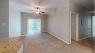 This single-story home in Spring, TX, offers a practical and comfortable layout with a neutral color palette throughout. The living area is carpeted and features a ceiling fan with light fixture, a sliding glass door that allows natural light to fill the space, and an open sightline toward the dining area and kitchen. The dining space connects seamlessly to the kitchen, which is designed in a galley configuration. It features dark espresso cabinetry, granite-style countertops, white subway tile backsplash, wood-look vinyl flooring, and black appliances including an electric range, microwave, refrigerator, and dishwasher.

The bedrooms are carpeted and include ceiling fans, windows for natural light, and closet access. The primary bedroom includes a spacious walk-in closet with built-in shelving on multiple walls, providing generous storage. The bathrooms feature wood-look vinyl flooring, dark vanity cabinetry with granite-style countertops, and large-format earth-toned tile surrounding the tub and shower areas. The overall design is cohesive, with consistent finishes tying together the functional, well-organized floor plan.