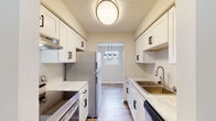 This single-floor unit has been thoughtfully updated with modern finishes throughout. The galley-style kitchen is a standout feature, outfitted with crisp white shaker cabinets accented by matte black hardware, light stone-look countertops, stainless steel appliances including a refrigerator, electric range, and dishwasher, and a stainless undermount sink. A flush ceiling fixture provides overhead lighting, while an opening at the far end leads into the dining area, which is illuminated by a stylish pendant light fixture and a window that brings in natural light.

The living and dining areas are open and airy, featuring wood-look plank flooring and neutral wall tones that create a clean, versatile backdrop. Windows along the exterior walls allow natural light to fill the space, and a wall-mounted air conditioning unit provides climate control.

The bedrooms are comfortably sized, each with wood-look flooring, neutral walls, and built-in closets with bifold doors offering practical storage. The full bathroom includes a soaking tub with shower, a white vanity, and matching wood-look flooring that ties seamlessly into the rest of the unit. Throughout the space, consistent finishes and a neutral palette create a cohesive and move-in ready environment.