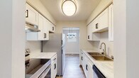 This single-floor unit has been thoughtfully updated with modern finishes throughout. The galley-style kitchen is a standout feature, outfitted with crisp white shaker cabinets accented by matte black hardware, light stone-look countertops, stainless steel appliances including a refrigerator, electric range, and dishwasher, and a stainless undermount sink. A flush ceiling fixture provides overhead lighting, while an opening at the far end leads into the dining area, which is illuminated by a stylish pendant light fixture and a window that brings in natural light.

The living and dining areas are open and airy, featuring wood-look plank flooring and neutral wall tones that create a clean, versatile backdrop. Windows along the exterior walls allow natural light to fill the space, and a wall-mounted air conditioning unit provides climate control.

The bedrooms are comfortably sized, each with wood-look flooring, neutral walls, and built-in closets with bifold doors offering practical storage. The full bathroom includes a soaking tub with shower, a white vanity, and matching wood-look flooring that ties seamlessly into the rest of the unit. Throughout the space, consistent finishes and a neutral palette create a cohesive and move-in ready environment.
