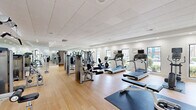 Located at Danville Park Drive SW in Decatur, Alabama, this fitness center offers a spacious, single-floor layout designed to accommodate a comprehensive range of workout activities. The open floor plan is finished with smooth hardwood-style flooring throughout, providing a clean and functional surface ideal for both equipment use and mat-based exercises.

The facility is outfitted with a robust selection of cardio equipment, including multiple treadmills, elliptical trainers, stationary bikes, and a recumbent cycle. A dedicated strength training area features several multi-function cable and weight machines suited for targeting various muscle groups, complemented by a free weights station with a full dumbbell rack. Exercise mats are positioned throughout for stretching and floor workouts.

Large windows along the exterior walls allow ample natural light to fill the space while offering views of the surrounding greenery, creating an energizing atmosphere. Full-length mirrors line multiple walls, visually expanding the room and providing functional feedback during workouts. Recessed lighting and a drop ceiling with integrated ventilation ensure a comfortable indoor environment year-round.

Motivational wall graphics and a wall-mounted flat-screen television add to the engaging ambiance. A clearly posted fitness center rules board is visible near the entrance, and access is provided through glass-paned double doors. The overall design is clean, modern, and well-maintained, making it a fully functional community fitness facility.