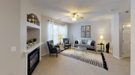 This two-story model home offers three bedrooms and two and a half bathrooms across a generously sized, thoughtfully designed floor plan. The layout is spread across two levels, providing clear separation between living and sleeping areas.

The living room is a welcoming space featuring plush carpeting, a ceiling fan with lighting, a fireplace, and a built-in shelving niche. Large windows with sheer curtains allow natural light to fill the room. Adjacent to the living area, the dining space features a bold teal accent wall and a large window, creating a vibrant yet intimate setting.

The kitchen is well-equipped with white shaker-style cabinetry, granite-look countertops, stainless steel appliances including a refrigerator, electric range, and built-in microwave, plus a central island offering additional prep space. Wood-style flooring runs throughout the kitchen.

The bedrooms are carpeted and feature ceiling fans. Each room is comfortably sized with ample wall space. The full bathrooms include white vanity cabinetry, large mirrors, and shower-tub combinations with wood-style flooring, while a half bath serves the common areas. Neutral gray tones throughout create a clean, cohesive aesthetic.