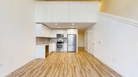 Located at 1255 Harrison St in Seattle, WA, this two-story residence offers a thoughtfully designed layout spread across two floors. The main level serves as the heart of the home, combining the living room, dining area, and kitchen into a cohesive open-concept space. The modern kitchen is outfitted with sleek, high-gloss white cabinetry, a tile backsplash, stainless steel appliances including a refrigerator, range, microwave, and dishwasher, and light wood-style flooring that extends seamlessly throughout the level. Tall windows on the main floor invite abundant natural light and provide views of the surrounding streetscape and greenery. A den and multiple closets add practical flexibility to the lower level, complemented by a full bathroom with a soaking tub and subway tile surround. A staircase with clean white railings leads to the upper floor, where the spacious primary bedroom awaits, featuring a ceiling fan, additional windows with natural light, and a second full bathroom nearby. The upper level also offers an open loft-style landing with a railing overlooking the stairwell. Warm wood-tone flooring, recessed lighting, and a crisp white palette create a bright, clean ambiance throughout this efficiently designed Seattle home.