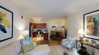 This single-floor residence offers a thoughtfully designed open-concept layout that seamlessly connects the living, dining, and kitchen areas. The kitchen is a standout feature, showcasing rich cherry wood cabinetry, granite-style countertops, stainless steel appliances including a refrigerator, range, and built-in microwave, and a peninsula island with additional seating — ideal for casual dining or entertaining. Track lighting illuminates the space effectively, complementing the wood-style flooring that extends throughout the main living areas. The open living room is bright and airy, featuring crown molding, plush carpeting, and sliding glass doors that invite natural light. A separate dining area provides an intimate setting beneath a stylish globe pendant light, accented by bold blue artwork. The bedrooms are generously sized with carpeted floors, large windows with curtain panels, and ample closet space. One bedroom features an elegant four-poster bed frame, adding a refined touch. The bathrooms are well-appointed, each featuring a tub-shower combination with tile surround, wood-style flooring, and warm accent walls. A hallway bathroom includes a rich cherry vanity with a white countertop. The overall palette of warm neutrals and blue accents creates a cohesive and inviting ambiance throughout.