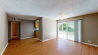 Located in San Marcos, California, this single-floor residence offers a well-organized layout designed for comfortable everyday living. The open living area is finished with warm hardwood-style flooring and features a ceiling fan, textured ceiling, and a large sliding glass door that floods the space with natural light and provides direct access to an outdoor patio overlooking lush greenery. The adjacent galley-style kitchen is efficiently designed with ample warm-toned wood cabinetry, dark granite-style countertops, a double-basin sink, and white appliances, including a refrigerator and range. A window at the end of the kitchen brings in additional natural light. The bedrooms are carpeted and offer a quiet, comfortable atmosphere, each with windows that provide views of the surrounding landscape. One bedroom features mirrored sliding closet doors, adding a sense of depth to the space. The bathroom is clean and functional, equipped with a single-sink vanity with dark countertops, wood cabinetry, and a walk-in shower. Throughout the unit, neutral warm-beige tones on the walls create a cohesive and inviting ambiance, making this a practical and comfortable residence in a convenient Southern California location.