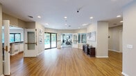 Located at 2775 Stowmarket Ave in Rockford, Illinois, this single-story community amenity center offers a thoughtfully designed layout that caters to both recreation and social gathering. The space is organized across a generous footprint, with distinct areas flowing seamlessly into one another via a connecting hallway.

The fitness center is a standout feature, outfitted with a variety of cardio and strength-training equipment including rowing machines, stationary bikes, free weights, and weight benches. Large windows line the walls, flooding the room with natural light and offering views of the surrounding greenery. A wall-mounted mirror expands the sense of space, while durable rubber flooring and a mounted TV complete the well-equipped environment.

The combined dining, kitchen, and living area serves as the social hub of the facility. The kitchen features white cabinetry, dark countertops, a bar-style peninsula with seating, and a pool-facing window that brings in abundant natural light. The adjacent dining area includes high-top tables and chairs, accented by warm hardwood flooring. The living room area is bright and open, anchored by a fireplace console and tasteful wall art, with direct access to the outdoor pool deck.

The welcoming entryway hallway features hardwood floors, glass double doors, and clean neutral tones. The exterior showcases a fenced outdoor pool surrounded by lounge chairs, a concrete deck, and mature landscaping.