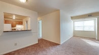 Located at 18 Tall Pine Dr in Hampton, Virginia, this single-floor home offers a clean, functional layout designed for comfortable everyday living. The main living area is spacious and open, featuring wall-to-wall carpet flooring in warm neutral tones that add a cozy feel to the space. Crisp white walls and standard ceiling height contribute to a bright, airy atmosphere throughout.

A standout feature of the living area is the pass-through window connecting directly to the kitchen, offering convenient sightlines and an open feel between the two spaces. The kitchen is partially visible through the pass-through, showcasing dark countertops that provide a subtle contrast to the light-toned cabinetry and walls.

A central hallway extends from the main living area, providing access to the additional rooms of the home and contributing to an efficient and straightforward floor plan. Natural light filters into the living space through a window, keeping the interior feeling fresh and welcoming. The overall design is practical and well-maintained, making this a solid, move-in ready home in the Hampton, Virginia area.