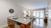 Located at 404 W Smith St in Greensboro, NC, this well-appointed 2-bedroom, 2-bathroom residence offers a thoughtfully designed single-floor layout. The open-concept kitchen and living area serves as the heart of the home, showcasing polished concrete floors, crown molding, and abundant natural light streaming through French doors that lead to a private balcony. The kitchen features rich wood cabinetry, granite countertops, a subway tile backsplash, stainless steel appliances, and a peninsula with bar seating that flows seamlessly into the dining and living spaces. The living room is bright and airy, with generous proportions and elegant crown molding details. The spacious primary bedroom impresses with vaulted ceilings, a ceiling fan, plush carpeting, and direct access to an en-suite bathroom. The second bedroom also features a ceiling fan and plush carpet, along with a window that fills the room with natural light. Both bathrooms are finished with granite vanity countertops, wood cabinetry, and tile flooring. A connecting hallway ties each space together, completing this cohesive and comfortable layout ideal for everyday living in downtown Greensboro.