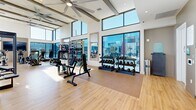 Located in Temecula, CA, this modern fitness center offers a generously sized, single-floor workout facility designed to inspire and accommodate a full range of exercise routines. The space is defined by its striking architectural design, featuring soaring double-height ceilings with exposed beams and large ceiling fans that maintain airflow throughout. Floor-to-ceiling windows and glass doors wrap around much of the perimeter, flooding the interior with abundant natural light and offering sweeping views of the surrounding mountains and outdoor areas — creating an energizing atmosphere for every workout.

Underfoot, smooth light wood-tone flooring runs throughout the space, lending a clean and contemporary aesthetic. The layout is thoughtfully organized to accommodate both cardio and strength training zones. Cardio equipment includes stationary bikes, treadmills, and other aerobic machines, while the strength training area is outfitted with cable machines, cable crossover systems, weight benches, and a full rack of dumbbells ranging across various weights. Wall-mounted mirrors are strategically placed to enhance the sense of space and support form monitoring during exercise.

Large sliding glass doors provide direct access to an outdoor area, seamlessly connecting indoor and outdoor environments. Mounted flat-screen displays add a modern touch, supporting interactive training experiences. The overall ambiance is bright, open, and contemporary, making this fitness center a premium wellness destination.