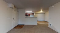 Located at 352 North Beck Road in Post Falls, Idaho, this single-floor unit offers a functional and comfortable layout designed for everyday living. The open-concept living area is finished with plush neutral carpeting and features a glass patio door fitted with vertical blinds, allowing natural light to fill the space. A wall-mounted heating unit and multiple outlets make the living area practical and ready for furnishing.

The kitchen is positioned behind a half-wall peninsula that doubles as a breakfast bar, creating a natural separation between the living and cooking spaces. Rich dark-wood cabinetry pairs with light marbled countertops, and the kitchen is equipped with stainless steel appliances including a refrigerator, over-the-range microwave, and a coil-top range. The kitchen floor features warm wood-look hard surface flooring, which continues into the hallway beyond.

The hallway connects the main living spaces to the private areas of the unit, with paneled doors leading to additional rooms and closet storage. A dedicated laundry area houses a full-size front-loading washer and dryer alongside a water heater, providing added convenience. The overall aesthetic throughout the unit is clean and neutral, with light gray walls, white trim, and a consistent use of warm-toned flooring and cabinetry that creates a cohesive, welcoming ambiance.