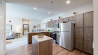 This 2-bedroom, 2-bathroom unit at Hawk Ridge Trail in Lake Saint Louis, Missouri, offers a thoughtfully designed single-story layout with contemporary finishes throughout. The open-concept kitchen serves as a central highlight, featuring taupe shaker-style cabinetry, granite countertops, a central island with additional prep space, and a full suite of stainless steel appliances including a refrigerator, range, and microwave. Warm-toned hardwood-style flooring runs through the kitchen and connects seamlessly to the surrounding living areas.

The living room is bright and comfortable, with plush carpeting, neutral walls, and multiple windows that invite natural light and outdoor views. A glass-paned door provides direct exterior access, enhancing the airy feel of the space.

Both bedrooms are carpeted and well-sized, offering ample room for furnishings. The primary bedroom includes a closet and opens to an en-suite bathroom. The two bathrooms differ in configuration: one features a walk-in glass shower with hardwood-style flooring, while the other offers a full soaking tub and shower combination, both appointed with granite vanity tops and taupe cabinetry consistent with the kitchen's design aesthetic.