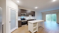 Located at 9800 Diffley Ct in Inver Grove Heights, MN, this 2-bedroom, 1-bathroom residence offers a well-designed single-level layout with modern finishes throughout. The open kitchen is a standout feature, showcasing dark espresso cabinetry, white quartz-style countertops, stainless steel appliances including a refrigerator, range, microwave, and dishwasher, and light hardwood-style flooring that extends into the living area. A kitchen island with built-in wine storage adds both function and style. The living room is bright and inviting, featuring a sliding glass door that opens to a balcony with lush outdoor views, allowing ample natural light to fill the space. Both bedrooms are carpeted for comfort; the primary bedroom includes a walk-in closet with wire shelving and direct access to the full bathroom. The second bedroom features a large window with tranquil tree-line views and a ceiling fan. The bathroom is finished with a dark wood vanity, white countertop, tub-shower combination with a curved rod, and hardwood-style flooring. Neutral wall tones and clean white trim create a cohesive, contemporary aesthetic throughout this well-appointed residence.
