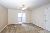 This single-floor unit offers a practical and straightforward layout connecting the main living spaces efficiently. The living area is generously sized, finished with wall-to-wall carpet and neutral-toned walls that create a clean, understated atmosphere. A ceiling fan is centrally mounted overhead, and a window along one wall admits natural light. A tiled entryway near the front door transitions smoothly into the carpeted space.

The kitchen is accessible directly from the living area via a pass-through counter with dark speckled countertops. Light wood cabinetry lines the upper and lower walls, providing ample storage, while a stainless steel sink sits beneath the upper cabinets. The kitchen floor is finished with neutral tile. Track lighting illuminates the space from above, and a full-size refrigerator is included.

The bedroom is a comfortable, well-proportioned room with wall-to-wall carpet, a ceiling fan, and a window fitted with blinds that allows natural light to filter in. The walls carry the same warm neutral tone found throughout the unit, maintaining a consistent aesthetic.

The bathroom includes a soaking tub with tiled surround, a toilet, tile flooring, and dark countertop vanity with light wood cabinetry, consistent with the kitchen finishes.