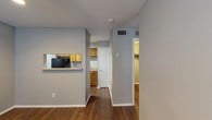 This single-story unit offers a practical and cohesive layout highlighted by warm wood-look flooring and neutral gray walls that carry consistently through each space. A central hallway connects the key areas of the unit, providing a clear and organized flow from room to room.

The galley-style kitchen is efficiently designed, featuring warm wood cabinetry on both sides, light-toned countertops, and a full suite of black appliances including a coil-top range, refrigerator, and dishwasher. A pass-through window opens the kitchen toward the adjacent living area, enhancing connectivity between the two spaces. The living area is generously proportioned, with a ceiling fan with light fixture, recessed lighting, a window fitted with blinds for natural light control, and built-in wall shelving that adds a functional decorative element.

Two bedrooms are present, each featuring wood-look flooring and textured ceilings. One bedroom benefits from a window with blinds and additional natural light, while a walk-in closet is accessible from the hallway. The full bathroom includes a tiled tub-shower combination, a single-sink vanity with a speckled countertop, and a mirror. Textured ceilings are found throughout the unit, and HVAC vents provide climate control across all rooms.