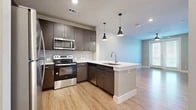 This well-designed 1-bedroom, 1-bathroom unit offers a functional and modern layout across a single floor. The open-concept kitchen and living area serves as the heart of the space, featuring rich dark-toned cabinetry, a subway tile backsplash, and a full suite of stainless steel appliances including a refrigerator, electric range, microwave, and dishwasher. A peninsula with a white quartz countertop and undermount sink provides additional prep space and doubles as a casual dining or entertaining area, accented by stylish pendant lighting overhead. Light hardwood flooring flows seamlessly throughout the entire unit, creating a cohesive and contemporary aesthetic. The living area is bright and airy, benefiting from a glass door that opens to a private outdoor area, allowing natural light to fill the room. A ceiling fan adds comfort and functionality. The bedroom offers a comfortable footprint, with two windows that invite natural light and provide outdoor views, along with its own ceiling fan. A dedicated closet provides convenient storage. The bathroom is finished with dark wood cabinetry, a white countertop vanity, an undermount sink with modern fixtures, and a tiled shower. Clean neutral wall tones and consistent flooring throughout contribute to the unit's cohesive, move-in-ready appeal.