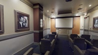 Located at 610 E Union St in Pasadena, California, this dedicated screening room offers a refined, cinema-inspired experience within a single-floor layout. The room is designed to evoke the golden age of Hollywood, with framed black-and-white photographs of classic film icons adorning the walls, creating an atmosphere of timeless elegance.

The seating arrangement features rows of generously sized lounge chairs and sofas upholstered in leather and patterned fabric, positioned to provide clear sightlines to the large projection screen mounted at the front of the room. A ceiling-mounted projector anchors the center of the space, supported by recessed and track lighting that allows for precise ambiance control.

The walls are finished in warm neutral tones accented by rich chocolate-brown architectural columns and a two-tone wainscoting detail, lending the room a polished, theatrical character. Dark wall-to-wall carpeting enhances the acoustic quality of the space while contributing to the immersive viewing environment. Decorative wall sconces provide a soft, flattering glow throughout.

Entry is through a distinctive set of double doors featuring circular porthole-style windows, adding a stylish focal point at the rear of the room. An ornate cabinet beneath the projection screen serves as a refined finishing detail. Altogether, this screening room delivers a sophisticated, fully appointed private cinema experience.