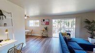 Located in Mountain View, California, this single-floor residence on Crisanto Avenue offers a well-organized and thoughtfully designed layout. The living room serves as the heart of the home, featuring warm hardwood-style flooring, a ceiling fan, and a large sliding glass door that opens onto a private balcony overlooking lush surrounding trees — filling the space with abundant natural light. The room comfortably accommodates a spacious sectional seating area and an entertainment setup complete with wall-mounted shelving.

Adjacent to the living room, the dining area is a cozy nook accented by decorative hexagonal wall art and a ceiling fan, with a compact round table and gold-accented chairs resting on the same continuous hardwood-style flooring.

The galley-style kitchen is efficiently laid out with white cabinetry, warm stone-toned countertops, and full appliances including a refrigerator, range, and dishwasher — maximizing functionality within a streamlined footprint.

The bedroom is a calm retreat, featuring a window with treetop views and a mirrored sliding closet door that adds depth to the room. The bathroom includes tile flooring, a vanity with ample storage, and a mirrored closet for added convenience. Throughout, the space maintains a clean, contemporary aesthetic with warm neutral tones.