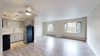 Located at 1969 SW Park Ave in Portland, Oregon, this single-floor unit offers a clean, contemporary living environment with thoughtful updates throughout. Light-toned hardwood-style flooring runs continuously across the main living areas, lending a bright and cohesive feel to the space. The open living room is generously proportioned, featuring multiple windows that frame lush, tree-lined outdoor views and allow ample natural light to fill the room. Baseboard heating units are present throughout, and ceiling fans are installed in several rooms for added comfort. The kitchen is efficiently designed with grey cabinetry, a white penny-tile backsplash, light countertops, stainless steel appliances including a range with microwave overhead, and track lighting above. The bedrooms are well-sized, each offering natural light from windows overlooking greenery, ceiling fans, and mirrored sliding closet doors for practical storage. The bathroom includes a shower-tub combination with clean white tile surround and tile flooring. A hallway connects the rooms in a straightforward, functional layout. The unit's neutral color palette and updated finishes create a bright, move-in ready atmosphere in a desirable Portland location.
