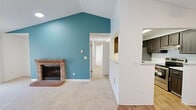 This well-appointed 3-bedroom, 1-bathroom home in Seattle, WA offers a thoughtfully designed single-floor layout with generous living space. The centerpiece of the home is a dramatic vaulted living room anchored by a classic brick fireplace and a bold teal accent wall, creating a warm and visually striking atmosphere. The soaring ceiling height amplifies the sense of openness, while a ceiling fan adds practical comfort. Plush carpeting runs throughout the living areas and bedrooms, contributing to a cozy feel.

The kitchen is efficiently laid out in a galley style, featuring dark cabinetry, light stone-look countertops, stainless steel appliances, and wood-look flooring illuminated by a skylight above. A pass-through connects the kitchen to the living area, enhancing the open flow. Three bedrooms offer neutral tones, carpeted floors, and ample wall space, with closet storage included.

The bathroom is clean and functional, featuring a dark wood vanity with a light countertop, a tub/shower combo, and wood-look flooring. A dedicated in-unit laundry area with a full-size washer and dryer adds convenience. A private balcony overlooks lush, mature evergreen trees, providing a peaceful Pacific Northwest backdrop.