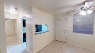 This single-story unit offers a well-organized layout that makes efficient use of its space. A defining architectural detail throughout is the painted white brick, which lends a distinctive, textured character to the living and entry areas. The main living and dining area features light tile flooring and is anchored by a ceiling fan with built-in lighting. A pass-through window with a granite ledge connects this space directly to the kitchen, promoting an open, communicative flow between the two areas.

The galley-style kitchen is equipped with dark cabinetry, granite countertops, and black appliances, including a refrigerator, electric range, dishwasher, and a sink. Tile flooring continues through the kitchen, which is illuminated by overhead lighting and accented by the same white brick wall visible throughout the unit.

The bedroom features carpet flooring, a ceiling fan with lighting, a window offering views of exterior greenery, and painted brick accent walls that maintain a consistent design language with the rest of the unit. A wall-mounted PTAC climate control unit is present in one of the rooms, ensuring year-round comfort. Natural light filters in through blinds-equipped windows in multiple areas of the unit.