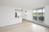 Located at 55 Tindale Court in Hamilton, Ontario, this single-floor unit showcases a clean, modern aesthetic throughout. Light wood-toned flooring runs continuously across the living areas and bedrooms, contributing to a cohesive and airy feel. Crisp white walls and natural light from multiple windows enhance the sense of openness.

The galley-style kitchen is well-appointed with high-gloss white cabinetry, quartz countertops, a white subway tile backsplash, and stainless steel appliances including a refrigerator and range. A peninsula counter connects the kitchen to the living area, offering casual seating or prep space. Recessed lighting illuminates the kitchen efficiently.

The living area features a large sliding glass door that opens to a balcony, framing attractive views of surrounding greenery and treetops. Baseboard heating runs along the perimeter of the main living spaces and bedrooms.

The bedrooms are generously proportioned, each benefiting from natural light and equipped with sliding-door closets. One bedroom includes an ensuite bathroom with a soaker tub, white tile surround, and quartz vanity. A dedicated laundry area houses a stacked washer and dryer unit with an adjacent workspace and a window overlooking the landscape.