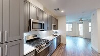 Located at 15501 North Dial Boulevard in Scottsdale, AZ, this thoughtfully designed single-floor unit offers a cohesive modern aesthetic across its living room, kitchen, and bathroom. The galley-style kitchen is a standout feature, showcasing dark gray shaker cabinetry, crisp white quartz countertops, a decorative arabesque tile backsplash, and a full suite of stainless steel appliances including a gas range, built-in microwave, dishwasher, and French door refrigerator. Warm-toned wood-look flooring runs continuously throughout the space, unifying each room with a clean, contemporary feel. The open living area is bright and airy, benefiting from multiple windows that invite natural light, a ceiling fan, and access to a private outdoor balcony. The bathroom continues the refined design language with a floating vanity in a coordinating gray finish, white quartz countertop, a lighted mirror, and wood-look flooring. Recessed lighting and neutral white walls enhance the sense of openness throughout. The unit also features a convenient entry area with a white panel door and dedicated storage cabinetry, adding practical functionality to the polished interior design.