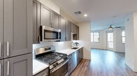 Located at 15501 North Dial Boulevard in Scottsdale, AZ, this thoughtfully designed single-floor unit offers a cohesive modern aesthetic across its living room, kitchen, and bathroom. The galley-style kitchen is a standout feature, showcasing dark gray shaker cabinetry, crisp white quartz countertops, a decorative arabesque tile backsplash, and a full suite of stainless steel appliances including a gas range, built-in microwave, dishwasher, and French door refrigerator. Warm-toned wood-look flooring runs continuously throughout the space, unifying each room with a clean, contemporary feel. The open living area is bright and airy, benefiting from multiple windows that invite natural light, a ceiling fan, and access to a private outdoor balcony. The bathroom continues the refined design language with a floating vanity in a coordinating gray finish, white quartz countertop, a lighted mirror, and wood-look flooring. Recessed lighting and neutral white walls enhance the sense of openness throughout. The unit also features a convenient entry area with a white panel door and dedicated storage cabinetry, adding practical functionality to the polished interior design.