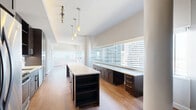 Located in the heart of downtown Dallas, this one-bedroom, one-bathroom residence offers a well-designed open-concept layout that seamlessly connects the kitchen and living area. Light hardwood flooring runs throughout the main living spaces, complemented by neutral tones and clean white trim that create a bright, modern atmosphere. Expansive floor-to-ceiling windows frame striking panoramic views of the Dallas skyline, flooding the living area with natural light.

The kitchen is a standout feature, equipped with rich dark-wood cabinetry, stainless steel appliances including a full-size refrigerator, range, and microwave, and a generous island with a crisp white countertop and pendant lighting overhead. A window-side counter offers additional workspace with skyline views.

The spacious bedroom is finished with plush carpet, a ceiling fan, and direct access to the en-suite bathroom. The bathroom is elegantly appointed with large-format tile, a sleek dark-wood vanity, white countertop, a glass-enclosed shower, and a separate soaking tub. A stacked washer and dryer unit is conveniently accessible from the bathroom.

A dedicated utility room and thoughtful storage complete this well-appointed urban residence, ideal for those seeking contemporary city living in Dallas.