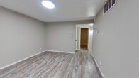 This single-story home in Dallas, Texas offers a thoughtfully updated interior with a cohesive, modern design. Light-toned wood-look flooring runs consistently throughout the living areas and bedrooms, complementing the neutral gray wall palette and crisp white trim to create a clean, contemporary feel.

The open layout connects the living area to the kitchen, which has been updated with white shaker-style cabinetry accented by matte black hardware, light granite-look countertops, and stainless steel appliances including a refrigerator and electric range. Flush-mount ceiling lights illuminate the space effectively.

Both bedrooms are comfortably proportioned, featuring the same wood-look flooring and neutral gray walls. One bedroom includes a ceiling fan with a window dressed in white blinds, while the other is fitted with a flush-mount light and an access panel. Natural light filters in through the windows, adding brightness to each room.

The bathroom is finished with a marble-patterned tile surround in the tub/shower combination, paired with matte black fixtures and hardware. White cabinetry and matching flooring continue the home's consistent design language, resulting in a polished, move-in ready space.