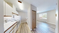 Located at 334 Wells Ave S in Renton, Washington, this one-bedroom, one-bathroom unit offers a thoughtfully utilized single-floor layout. Light-toned hardwood flooring runs throughout the entire space, creating a cohesive and clean aesthetic from room to room.

The open living area connects seamlessly to a compact kitchen tucked along one wall, featuring white cabinetry and a built-in stovetop. A small breakfast bar ledge adds a practical touch to the kitchen-living transition. The layout includes a dedicated entryway corridor with a utility panel, lending an organized flow into the main living space.

The spacious bedroom is a standout feature, offering generous proportions relative to the overall footprint. It is equipped with a full-width mirrored sliding closet with gold-toned framing, which also amplifies natural light from the window overlooking the surrounding neighborhood. A baseboard heater beneath the window provides consistent warmth.

The bathroom is efficiently designed with light wood-toned cabinetry, a single vanity with under-sink storage, and hard flooring that mirrors the rest of the unit. Accessibility grab bars are present near the toilet area. Natural light enters through a window fitted with horizontal blinds, keeping the space bright and airy. Overall, the unit presents a clean, move-in-ready environment with a neutral palette throughout.