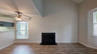 Located at 101 Meadowood St in Greensboro, NC, this one-bedroom, one-bathroom unit offers a well-designed layout across a single floor. The living room is an immediate standout, boasting soaring vaulted ceilings that create an airy, open atmosphere and a classic wood-burning fireplace as the focal point. Hardwood-style flooring runs throughout the living area, complemented by a ceiling fan and natural light streaming in through multiple windows. The kitchen features gray cabinetry, light countertops, a white subway tile backsplash, and black appliances including an electric range — all finished with matching hardwood-style flooring for a cohesive look. The spacious bedroom offers plush carpeting, a sliding glass door that opens to an outdoor view, and convenient access to a dedicated closet. A second carpeted room provides additional flexible living space with its own closet access. The bathroom includes a full tub and shower combination with clean white surround. Throughout the unit, neutral tones and practical finishes create a functional and comfortable living environment suited for everyday life in Greensboro.