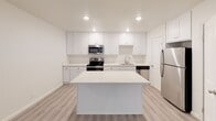 This single-floor unit at 8155 Cargill Ave in San Diego presents a clean, modern aesthetic defined by a bright white palette and light-toned luxury vinyl plank flooring that flows consistently throughout every room. The kitchen serves as a central highlight, featuring white shaker-style cabinetry extending to the ceiling for ample storage, white quartz countertops, a stainless steel appliance suite including a refrigerator, electric range, microwave, and dishwasher, and a central island that provides additional prep and gathering space. The open layout connects the kitchen seamlessly to the living area, which is illuminated by recessed lighting and a ceiling fan. The bedrooms maintain the same light, airy quality, each equipped with ceiling fans, closets with sliding or standard doors, and windows that invite natural light. The bathroom is well-appointed with a white vanity topped with a white countertop, a framed mirror, and a frameless sliding glass walk-in shower enclosure, all complemented by the same wood-look flooring. Throughout the unit, crisp white walls and clean finishes create a cohesive, move-in-ready environment suited to a variety of living arrangements.