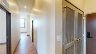 This single-floor unit offers a thoughtfully designed layout with a clean, contemporary aesthetic throughout. The kitchen serves as a central highlight, featuring a large island with a striking stone countertop, an undermount sink with a matte black faucet, and gray shaker-style cabinetry complemented by a mosaic tile backsplash. Stainless steel appliances, including a refrigerator, range, and microwave, complete the space, while industrial-style pendant lights and large windows framing urban skyline views add character and natural light.

The hallway connects the living areas to the bedrooms and bathrooms, with warm hardwood-style flooring running throughout. A louvered closet door provides practical storage access from the corridor. The bedrooms are bright and airy, each benefiting from large, black-framed windows that capture expansive city views and allow generous sunlight to flood the rooms.

Two bathrooms mirror each other in style, each featuring rich walnut-toned cabinetry, white countertops, and a glass-enclosed shower. One bathroom is distinguished by a backlit vanity mirror, adding a refined touch. Neutral tile flooring and matte black hardware accents unify both spaces, contributing to the unit's cohesive modern design.