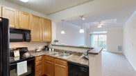 This one-bedroom, one-bathroom unit in West Columbia, SC offers a well-designed single-floor layout that maximizes functionality and comfort. The open-concept kitchen flows directly into the living room, connected by a peninsula with dark laminate countertops, warm honey-toned cabinetry, pendant lighting, and black appliances including a refrigerator, dishwasher, and range. The living room is a standout space, featuring a tray ceiling with crown molding, a ceiling fan, plush carpeting, and sliding glass doors that open to a private balcony with outdoor views. The carpeted bedroom is comfortably sized, featuring a tray ceiling, a large window with natural light, and ample wall space. The bathroom includes a wood-toned vanity with a granite-style countertop, a large mirror, and wood-look vinyl flooring. A dedicated laundry area accommodates a full-size washer and dryer with overhead wire shelving for additional storage. The unit also includes a hallway and closet, providing practical organization. Throughout, the space maintains a clean, neutral palette that creates a bright and welcoming ambiance, suitable for everyday living in a convenient West Columbia location.