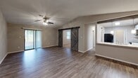 Located at 4035 Kessler Ave in Garden City, Georgia, this single-floor home offers a well-organized layout with a variety of functional spaces. The living area features light wood-look flooring, vaulted ceilings with recessed lighting, and a ceiling fan, creating an open and airy atmosphere. The kitchen is thoughtfully updated with white shaker-style cabinetry, granite-look countertops, a subway tile backsplash, black appliances including an electric range and microwave, and a stainless steel sink—all complemented by the same light hardwood flooring. A decorative barn door accent adds a modern touch to the common areas. The bedrooms are carpeted for comfort, each equipped with ceiling fans and closets with wire shelving for ample storage. The bathroom features a granite-topped vanity with white cabinetry, a large mirror, and a full tub-shower combination with brushed nickel fixtures. A dedicated in-unit laundry area houses a washer with additional wire shelving above for storage. The enclosed porch, finished with white panel siding, blue carpet, and a sliding glass door, provides a versatile bonus space suitable for relaxation or recreation.