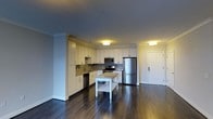 This single-floor residence offers a well-appointed open-concept layout that seamlessly integrates the kitchen and living areas into one cohesive space. The kitchen is a standout feature, showcasing crisp white cabinetry that extends to the ceiling, providing generous storage. A decorative tile backsplash adds texture and visual interest behind the range, while stainless steel appliances — including a refrigerator, range, microwave, and dishwasher — lend a modern, polished finish. A freestanding butcher block island offers additional prep space and flexibility. Crown molding along the ceiling adds a refined architectural touch, elevating the overall aesthetic. The rich, dark hardwood flooring runs throughout the space, creating a warm and grounded ambiance that contrasts elegantly with the light cabinetry. Flush-mount ceiling fixtures provide consistent, even lighting across the open area. The entry door is conveniently positioned adjacent to the kitchen, making the layout highly functional. The cool gray-toned walls complement the neutral palette, resulting in a clean, contemporary feel throughout the space.