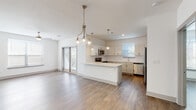 This single-floor unit presents a clean, modern aesthetic carried consistently throughout its layout. The open-concept living and kitchen area serves as the heart of the space, where warm wood-look flooring extends seamlessly underfoot. The kitchen is well-appointed with white shaker-style cabinetry, light quartz countertops, a subway tile backsplash, and a full suite of stainless steel appliances including a refrigerator, range, microwave, and dishwasher. A peninsula with pendant lighting provides additional workspace and separates the kitchen from the living area, which receives natural light through sliding glass doors leading to the exterior. Multiple bedrooms continue the cohesive design with wood-look flooring, neutral walls, and windows fitted with horizontal blinds. Each bedroom includes a ceiling fan for added comfort. Two full bathrooms mirror one another in style, each offering a single-sink vanity with white cabinetry and quartz countertop, a tub-shower combination, and matching wood-look flooring. A dedicated entry hallway with double doors provides practical storage. The overall ambiance is bright, clean, and move-in ready.