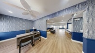 Located at 3333 N Michael Way in Las Vegas, NV, this single-floor community clubhouse offers a generously sized, open-concept layout designed for both comfort and functionality. The space is immediately distinguished by its striking interior design — bold navy blue wainscoting lines the lower walls, paired with an eye-catching blue-and-white botanical patterned wallcovering above, creating a cohesive and vibrant aesthetic throughout.

Light-toned hardwood-style flooring runs continuously across the entire space, enhancing the sense of openness and flow. Recessed lighting and palm-leaf ceiling fans are installed throughout, ensuring the space remains bright and well-ventilated.

The main lounge area features comfortable leather seating arranged around a woven rattan coffee table, ideal for relaxed gatherings. Adjacent to the lounge is a kitchenette equipped with white cabinetry, a stainless steel refrigerator, a countertop bar with bar stools, and ample prep space. A separate dining area accommodates a full dining table and chairs, bathed in natural light from large windows.

A dedicated private office provides a workstation with guest seating — well-suited for leasing or administrative functions. French doors at the rear open to an outdoor area, adding an inviting sense of connection to the exterior. The overall ambiance is polished, welcoming, and thoughtfully designed.