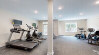This dedicated fitness center at 1-5 Soldier Hill Rd in Paramus, New Jersey, offers a well-equipped, single-floor workout facility designed to support a comprehensive exercise routine. The space is finished with durable, cushioned carpet flooring throughout, providing comfort underfoot during workouts, while neutral-toned walls and recessed lighting create a clean, focused environment.

The cardio section is generously stocked with multiple Spirit-brand treadmills and elliptical trainers, each paired with wall-mounted flat-screen monitors for an engaging workout experience. A row of stationary and recumbent bikes rounds out the cardio offerings. For strength training, the facility includes a multi-station cable and weight machine, a rack of dumbbells reflected by a large wall mirror, and a freestanding functional training rack.

Natural light filters in through multiple windows positioned along the walls, with a set of glass doors leading out to an adjacent outdoor deck area, adding an open, airy quality to the space. Structural support columns are neatly finished and blend seamlessly into the overall design. The layout is thoughtfully organized to provide ample floor space between equipment, ensuring ease of movement throughout. This fitness center delivers a practical, well-rounded facility suited for daily use.