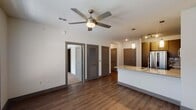 This well-appointed 1-bedroom, 1-bathroom unit in Houston, TX is designed with a modern aesthetic and functional open-concept layout. The main living area features rich hardwood-style flooring, neutral-toned walls, and a ceiling fan that promotes comfortable air circulation. The kitchen is a standout feature, equipped with stainless steel appliances including a refrigerator, range, microwave, and dishwasher. Dark wood cabinetry with sleek hardware pairs elegantly with light granite countertops and a subway tile backsplash. A peninsula with an undermount sink and pendant lighting above adds both workspace and a casual dining option. The bedroom is carpeted for comfort and includes a ceiling fan, a large window allowing natural light, and a built-in desk with shelving — ideal for a home workspace. The bathroom is thoughtfully designed with a granite-topped vanity, an undermount sink, stylish fixtures, and access to a walk-in closet. Hardwood-style flooring continues through the bathroom hallway, tying together the overall design. Multiple windows throughout the unit provide natural light and views of the surrounding exterior, contributing to a bright, welcoming ambiance.