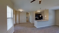 This single-story space features an open-concept layout that seamlessly connects the living area and kitchen, creating a spacious, airy feel. The flooring throughout is a warm wood-look material that adds continuity and a modern touch to the interior.

The kitchen is a standout feature, equipped with dark espresso-toned cabinetry that contrasts beautifully against light granite countertops. A central island with pendant lighting overhead serves as both a functional workspace and a natural gathering point. Black appliances, including a refrigerator and range with built-in microwave, complete the kitchen's contemporary look. A tile backsplash adds additional visual interest behind the range.

The living area is generously proportioned, with neutral-toned walls and a ceiling fan that promotes comfort and airflow. Recessed lighting supplements the natural light that filters in through the windows. A hallway visible from the main living space leads to additional rooms, providing a sense of depth and privacy within the layout. The overall ambiance is clean, modern, and move-in ready, appealing to those who value an open, functional living environment.