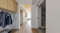 Located at 154 Broadway in Somerville, MA, this thoughtfully designed one-bedroom, one-bathroom unit offers an efficient and modern living experience across a single floor. The interior makes excellent use of its footprint, with light wood flooring flowing throughout and a warm natural-wood ceiling in the bedroom and kitchen area that adds architectural character.

The hallway entry features built-in overhead cabinetry and an open closet with a clothing rod, providing practical storage from the moment you step inside. A sleek sliding barn door with black hardware opens to the bathroom, which is finished with large-format stone-tile flooring and marble-style wall tile in the walk-in shower, creating a clean, spa-like aesthetic.

The kitchen is outfitted with light wood upper cabinetry, white lower cabinets, and white subway tile backsplash, integrating seamlessly into the open living and bedroom area. The primary bedroom is generously proportioned and benefits from multiple windows that bring in abundant natural light and views of the surrounding Somerville streetscape.

The living area accommodates a dining nook and lounge space, with white walls providing a bright, neutral canvas throughout. The overall ambiance is modern, minimal, and warm — a cohesive blend of natural materials and contemporary design well-suited for urban living.