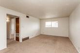 This single-story residence offers a practical, straightforward layout distributed across several interconnected rooms. The living area is generously proportioned, featuring neutral-toned wall-to-wall carpeting, a textured ceiling, and a horizontal window that admits natural light and outdoor views. A ceiling fan with an integrated light fixture serves an additional carpeted room, providing both ventilation and ambient lighting. Dark wood interior doors appear consistently throughout the unit, contributing a warm contrast against the white walls.

The kitchen is equipped with warm-toned wood cabinetry spanning both upper and lower sections, dark laminate countertops, a double basin sink, and a gas range. Tile flooring and a small recessed window add functionality and brightness to the workspace.

The bathroom includes a full tub-and-shower combination with white square tile surround, a vanity with a dark wood base, a large mirror, tile flooring, and a pendant light fixture suspended from a decorative chain — a distinctive detail within the space.

A spacious walk-in closet features dual-sided shelving and hanging rods, offering substantial storage capacity. The 3D floor plan view confirms a multi-room configuration with a connected, efficient flow throughout the single-floor layout.