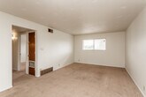 This single-story residence offers a practical, straightforward layout distributed across several interconnected rooms. The living area is generously proportioned, featuring neutral-toned wall-to-wall carpeting, a textured ceiling, and a horizontal window that admits natural light and outdoor views. A ceiling fan with an integrated light fixture serves an additional carpeted room, providing both ventilation and ambient lighting. Dark wood interior doors appear consistently throughout the unit, contributing a warm contrast against the white walls.

The kitchen is equipped with warm-toned wood cabinetry spanning both upper and lower sections, dark laminate countertops, a double basin sink, and a gas range. Tile flooring and a small recessed window add functionality and brightness to the workspace.

The bathroom includes a full tub-and-shower combination with white square tile surround, a vanity with a dark wood base, a large mirror, tile flooring, and a pendant light fixture suspended from a decorative chain — a distinctive detail within the space.

A spacious walk-in closet features dual-sided shelving and hanging rods, offering substantial storage capacity. The 3D floor plan view confirms a multi-room configuration with a connected, efficient flow throughout the single-floor layout.