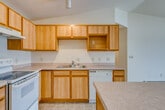 This single-floor residence offers a practical and functional layout with a well-connected open-concept design. The kitchen is equipped with warm honey-toned wood cabinetry, light countertops, tile flooring, a full suite of white appliances including a refrigerator, electric range, and dishwasher, plus a central island that provides additional workspace and storage. Track lighting overhead brightens the kitchen, which flows seamlessly into the expansive living and dining area. The living area features soft wall-to-wall carpeting, a ceiling fan, a fireplace, a wall-mounted air conditioning unit, baseboard heating, and a sliding glass door that opens to an outdoor balcony, filling the space with natural light. A dining area with a pendant light fixture connects the kitchen and living spaces. The bedrooms are carpeted and include baseboard heating and windows with blinds. The bathrooms feature tile flooring and warm wood cabinetry; the primary bathroom includes a dual-sink vanity with a large mirror and a shower area. A dedicated laundry room houses a full-size washer and dryer alongside a water heater, providing convenient in-unit utility. Overall, the space presents a clean, neutral palette with warm wood accents throughout.