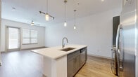 Located in Houston's vibrant 77007 corridor, this well-appointed one-bedroom, one-bathroom residence offers a thoughtfully designed open-concept layout. The combined kitchen and living area is anchored by a large center island with a white quartz countertop, an integrated sink, and a dishwasher. Gray shaker-style cabinetry pairs with stainless steel appliances — including a refrigerator, microwave, and range — while pendant lighting and a track light fixture add a modern touch. Light wood-look flooring runs throughout the main living space, which benefits from natural light through windows fitted with blinds and access to an exterior door. A ceiling fan completes the living area. The bedroom is carpeted for comfort and features a bright window with outdoor views and generous proportions. Two closets, including a walk-in equipped with wire shelving systems and built-in shelving units, provide ample storage. The bathroom is finished with large-format tile flooring, gray shaker vanity cabinetry, a white quartz countertop, an illuminated backlit mirror, and a walk-in shower, delivering a clean, contemporary aesthetic throughout.
